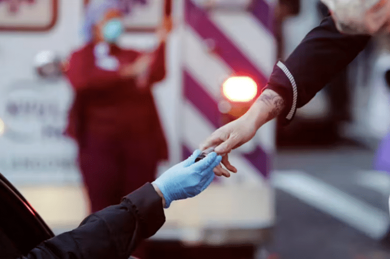 A hand with a blue surgical glove on it reaches up to a woman's bare hand.